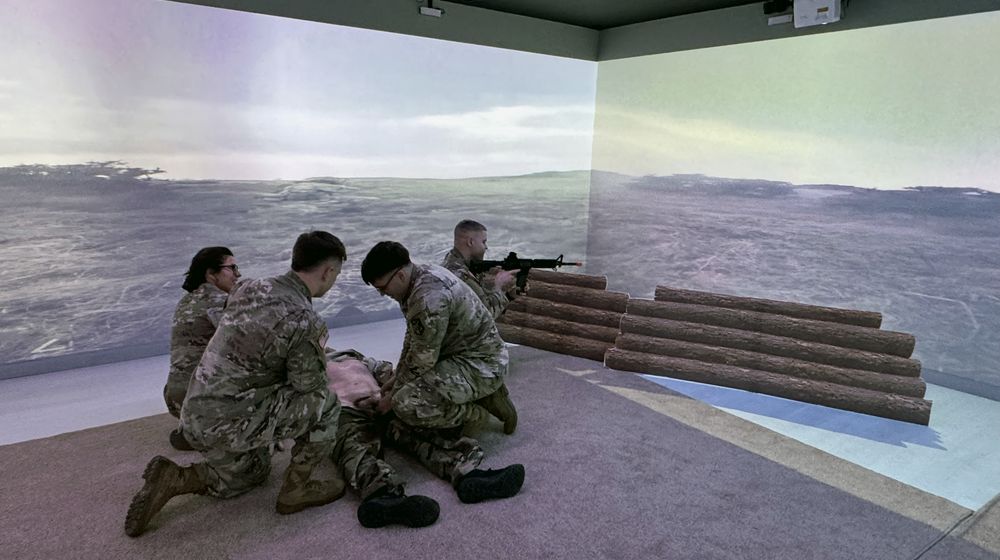 Soldiers treating a casualty under simulated fire inside a multi-wall projection training range